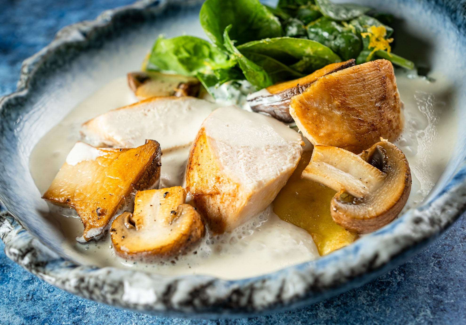 Keramikschüssel mit cremiger Soße, gebratenen Pilzscheiben und Hähnchenstücken, garniert mit frischem Gemüse. Das Gericht sieht reichhaltig und verlockend aus.